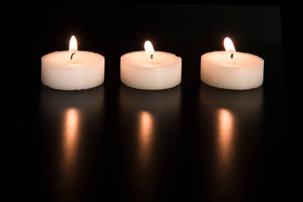 Three white burning tea lights in line with their reflection on a black background