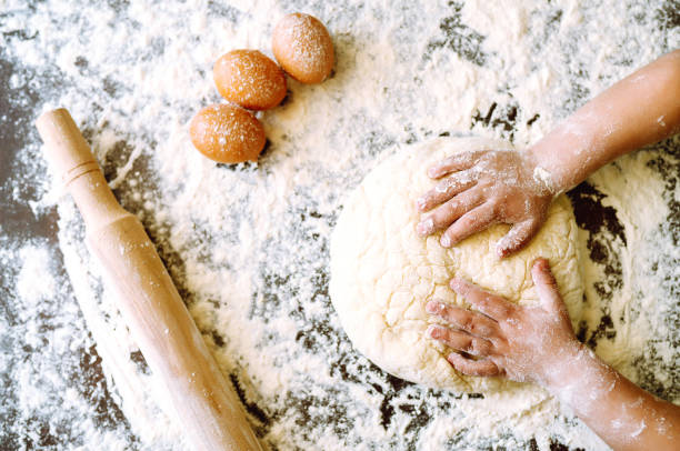 istock Children hands kneading dough for baking.  Kids hands, some flour, wheat dough and rolling pin on the dark table. Cookies for Christmas. 1286467649
