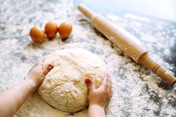 istock Children hands kneading dough for baking.  Kids hands, some flour, wheat dough and rolling pin on the dark table. Cookies for Christmas. 1286467663