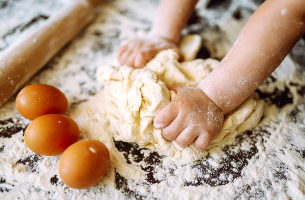istock Children hands kneading dough for baking.  Kids hands, some flour, wheat dough and rolling pin on the dark table. Cookies for Christmas. 1286467694