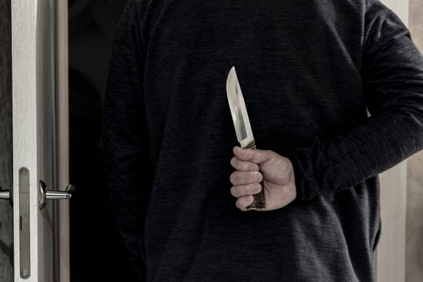 A man walks through the door to a dark room and holds a knife in his hand behind his back. A man walks through the door to a room and holds a knife in his hand behind his back. knife crime photos stock pictures, royalty-free photos & images