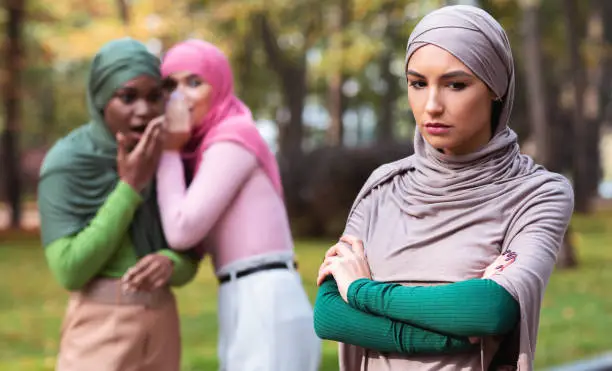 Photo of Bad Friends Talking About Unhappy Muslim Woman Standing Alone Outdoor