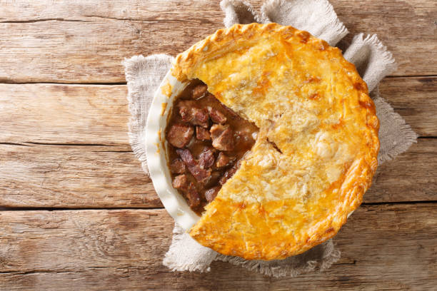 English beef steak pie with crispy puff pastry close-up in a baking dish. horizontal top view English beef steak pie with crispy puff pastry close-up in a baking dish on the table. horizontal top view from above savoury pie stock pictures, royalty-free photos & images