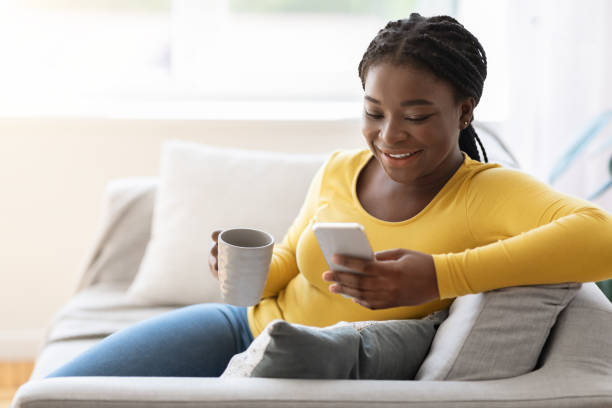 istock Weekend Leisure. Cheerful black female using smartphone and drinking tea at home 1286473225