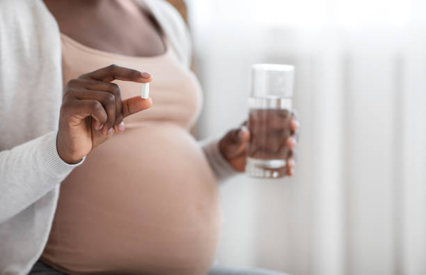 Supplements During Pregnancy. Unrecognizable Black Expectant Lady Holding Pill And Water Glass Supplements During Pregnancy. Unrecognizable Black Expectant Lady Holding Pill In Hand And Glass Of Water, Taking Maternity Vitamins For Health, Cropped Image With Selective Focus, Closeup folic acid stock pictures, royalty-free photos & images