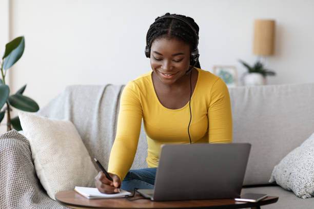 Online Education. Smiling Black Woman In Headset Studying With Laptop At Home Online Education Concept. Smiling Black Woman In Headset Studying With Laptop At Home And Taking Notes To Notepad, Enjoying Distance Learning, Watching Webinar In Internet And Noting Highlights masters degree photos stock pictures, royalty-free photos & images