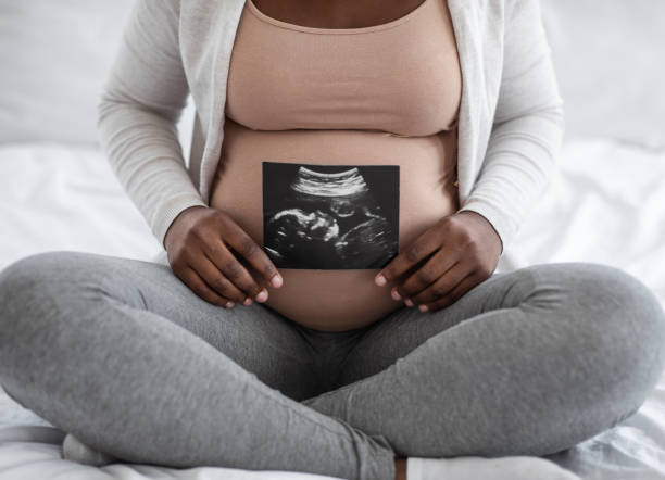 無法辨認的黑色孕婦展示她的嬰兒聲像照片， 坐在床上 - 腹部 圖片 個照片及圖片檔