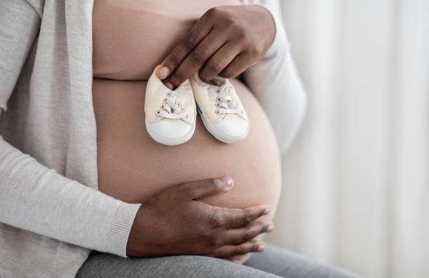 desired pregnancy. black pregnant woman embracing belly and holding small baby shoes - shoe women adult baby imagens e fotografias de stock