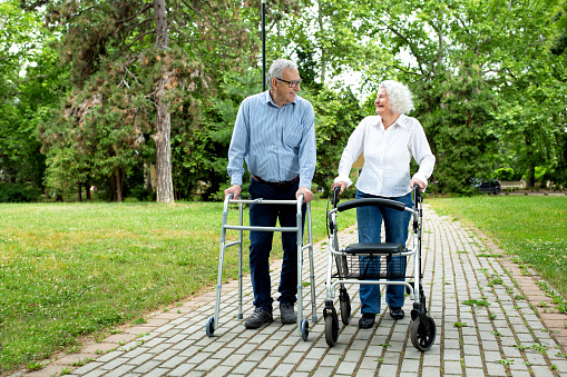 Elderly couple chatting and strolling in the park with a little help of walking equipment