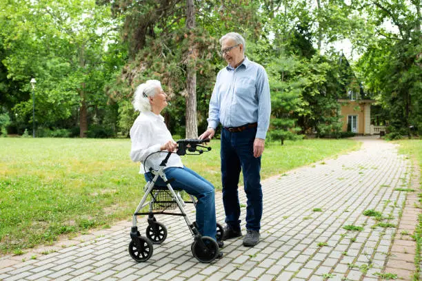 Senior woman sitting in her rolling walker being accompanied with a senior man in the park