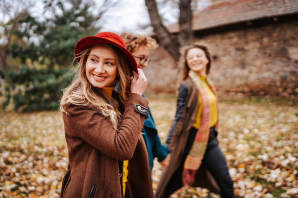 Three cheerful female friends walking and having fun in autumn park on beautiful sunny day