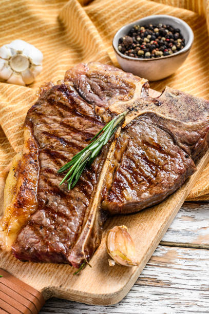 istock Grilled T bone steak on a chopping Board. Cooked tbone beef. White wooden background. Top view 1286487306