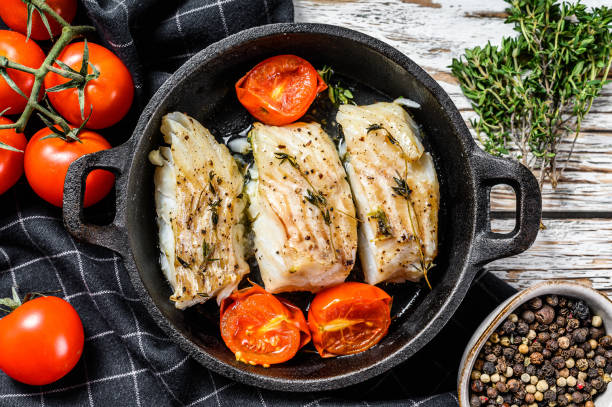 istock Fried cod fish fillet with spice in a cast iron pan.  White background. Top view. 1286487547