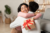自宅でクリスマスプレゼントを受け取る夫を抱きしめる喜びのアジアの妻