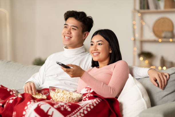 cônjuges asiáticos curtindo a véspera de natal assistindo tv na sala de estar - family sofa night indoors - fotografias e filmes do acervo