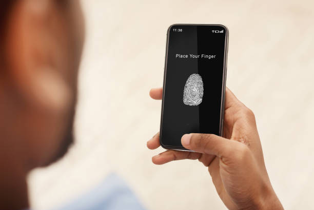 Man holding phone with fingerprint scanning app Biometric Identification Concept. Over The Shoulder View Of Black Man Holding Mobile Phone In Hand, Showing App For Fingerprint Scanning With A Zone To Touch With Thumbprint Icon On The Device Screen biometrics photos stock pictures, royalty-free photos & images