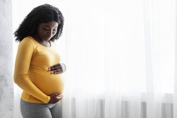 自宅で彼女のおなかを抱きしめる美しい妊娠中のアフリカの女性 - abdomen adult affectionate baby ストックフォトと画像