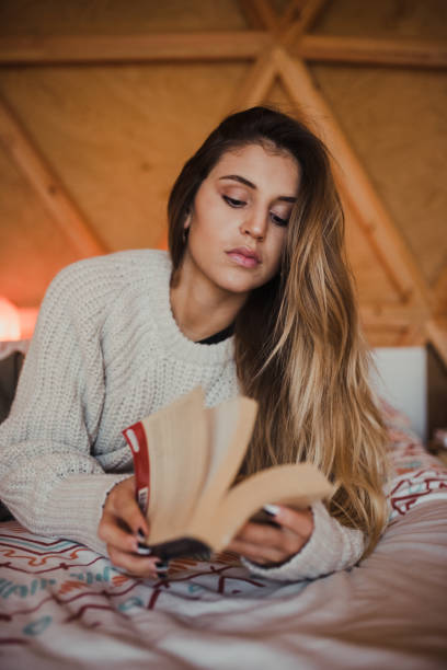 istock Young woman reading a book on a bed 1286490576