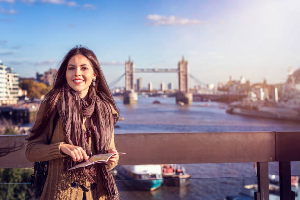 a female tourist in london holding a travel guide in front of the tower bridge, london - women travel destinations london england tourist imagens e fotografias de stock