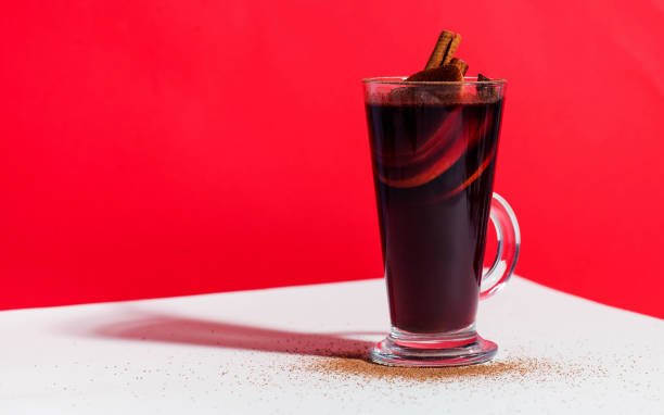 istock Mulled wine in a glass with a cinnamon stick on a red background with a hard light. Trending photo. Copy space. 1286495502