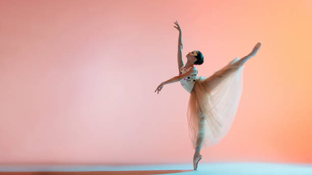 istock Young slim ballerina in light long dress is dancing on colored background with backlight 1286498598