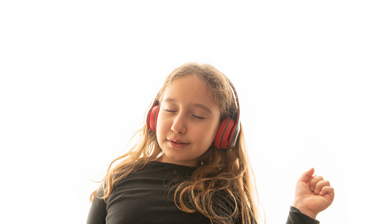 Little girl listens to music through headphones, a child dances to music on white background