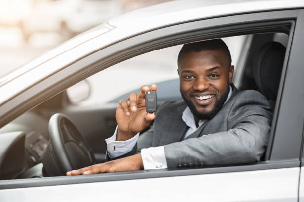 istock Happy black guy in suit holding key from new car 1286502661