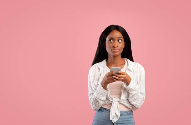 istock Young black lady holding smartphone and looking at blank space over pink studio background 1286502746