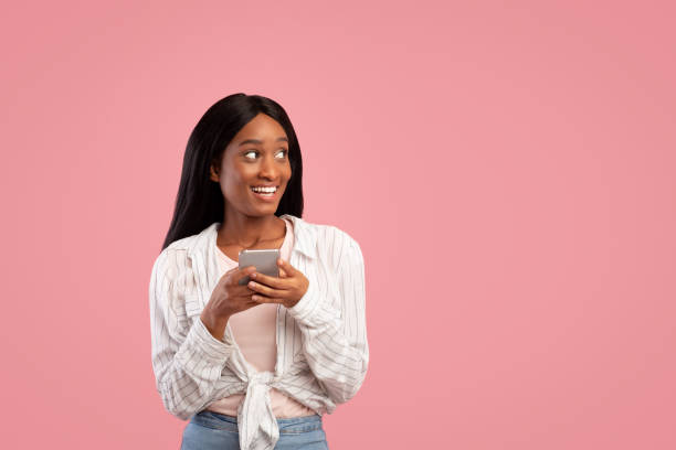 istock Millennial black woman with cellphone looking aside at empty space, pink studio background 1286502764