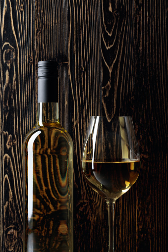 Bottle and glass of white wine on an old wooden background. Copy space.
