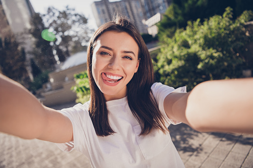 Photo portrait of girl showing tongue taking selfie holding with two hands in park.