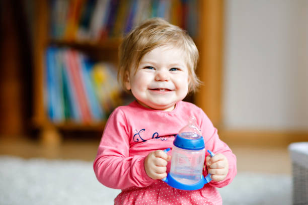 授乳ボトルを保持し、フォーミュラミルクや水を飲んでかわいい愛らしい女の赤ちゃん。赤ちゃんのための最初の食べ物。健康な赤ちゃんと子供のための哺乳瓶の概念 - female nurse 写真 ストックフォトと画像