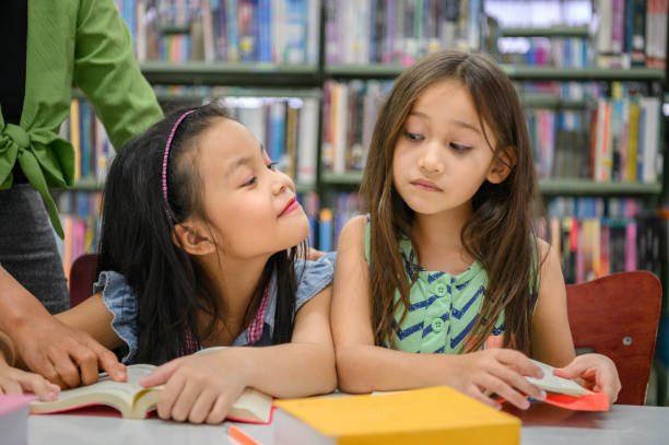 istock Two cute girls are jealous of each other while reading books in library while teacher teaching. People lifestyles and education. Young friendship and Kids relationship in school concept. Daycare theme 1286511221