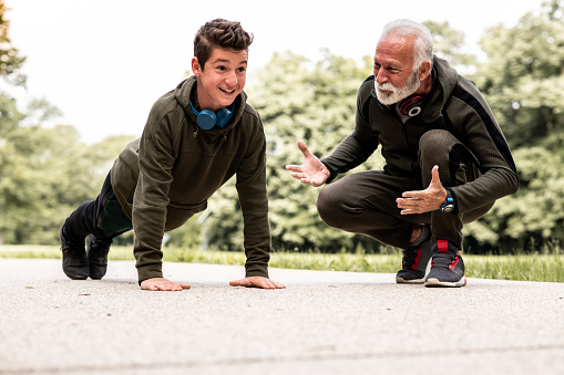 A senior athlete man is teaching his grandson how to do the push-ups properly: he should straighten his arms and look ahead and hold for a few seconds.