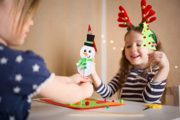 Photo of paper craft for kids. girls play with homemade toys snowman and christmas tree. create fun art for children. new year concept
