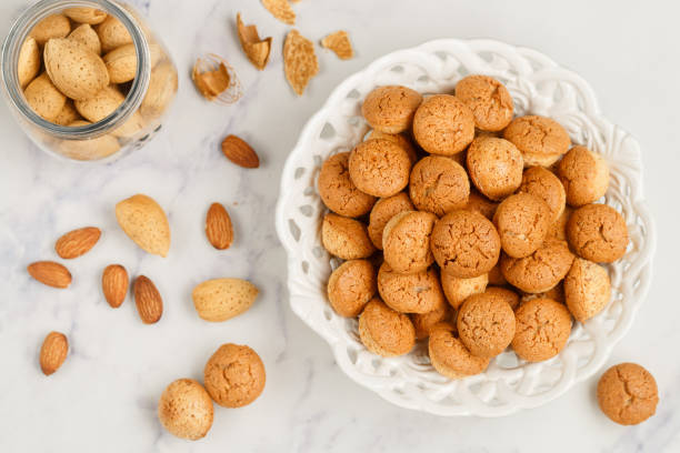 amaretti-traditionelle italienische mandelkekse in einem weißen teller auf einem marmor-top-blick hintergrund. amarettini kekse. selektiver fokus - biscotti stock-fotos und bilder