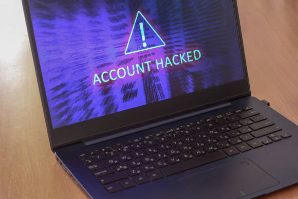 istock Laptop on the table and on a blue screen the text account is hacked. Warning triangular sign with exclamation mark symbol. Horizontal. 1286522841