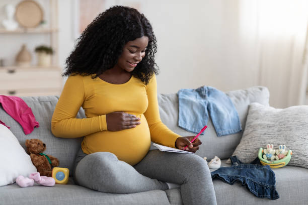 Happy pregnant woman sitting on sofa with notebook and pen