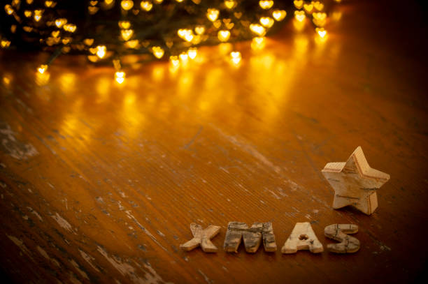 String lights with bokeh effect conjures up a beautiful Christmas atmosphere. In the Vodergrund there are letters that form the word XMAS and next to it is a small star made of wood.
