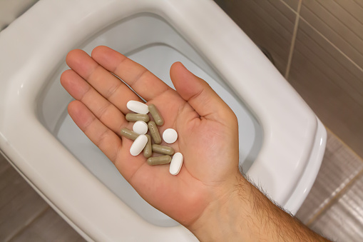 Male hand with medical tablets over toilet. Bellyache, constipation, diarrhea or food poisoning concept.