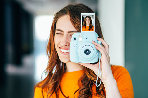 Smiling woman enjoying to take photos with instant camera