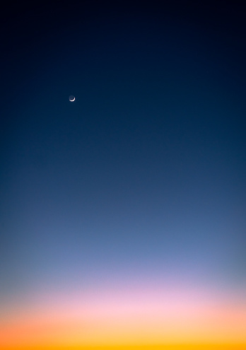 A graduated sky background at dusk, ranging from deep blue to orange by the horizon, with the crescent moon out.