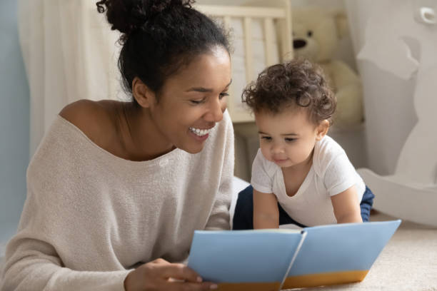 uśmiechnięta dwurasowa mama czyta książkę z niemowlęciem - baby book toddler reading zdjęcia i obrazy z banku zdjęć