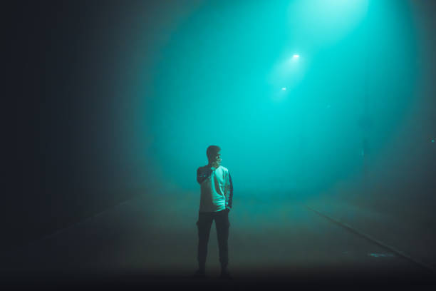 giovane in piedi da solo in una strada nebbiosa illuminata - fog road spooky mist foto e immagini stock