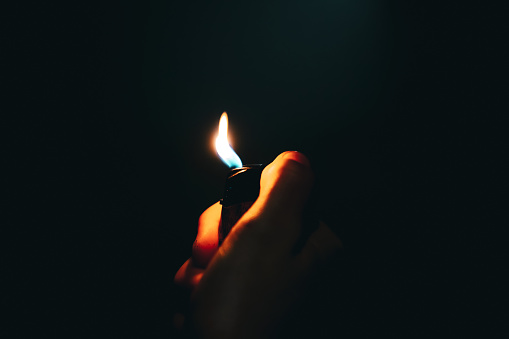Detail of hand lighting up a cigarette ligher at night. Selective focus on hand and burning flame.