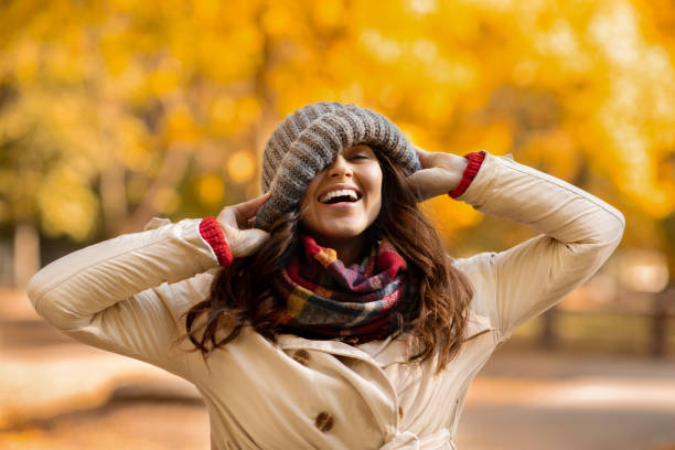 istock Playful young woman pulling down beanie hat on her face and laughing at park on warm autumn day 1286533760