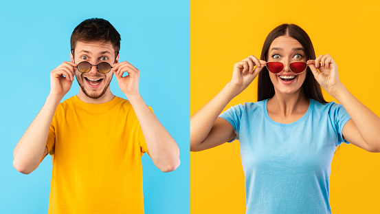 Wow. Portrait of man and woman posing at studio, taking off sunglasses, looking at camera in amazement and with surprised facial expression isolated on blue and yellow background. Unbelievable Sale