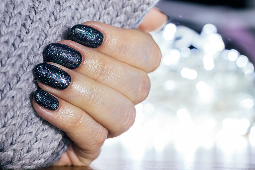 Female hand with gray knitted scarf and festive manicure - blue glittered nails at new year or Christmas party. Selective focus. Closeup view with copy space