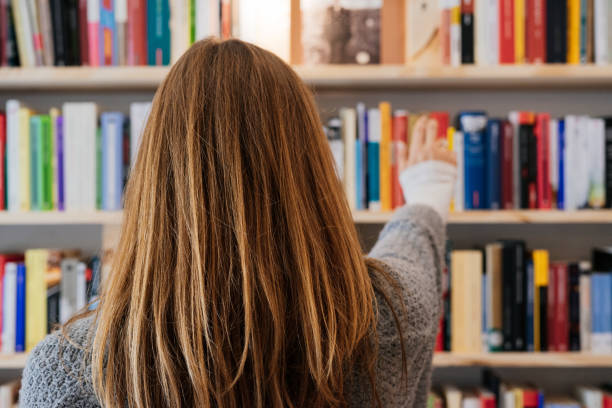 istock Young blonde woman on her back choosing a book from a bookcase. 1286540733