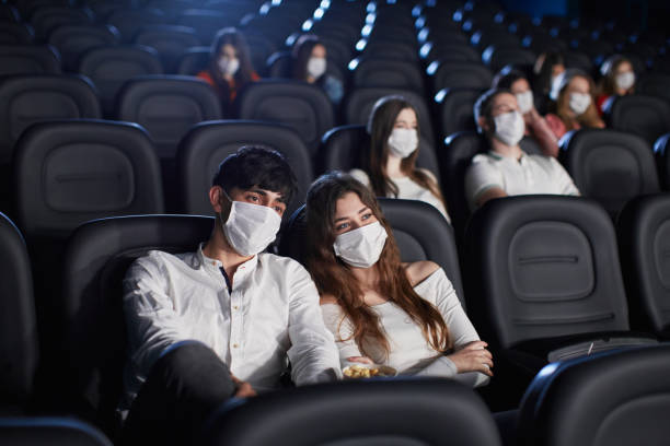 publikum mit gesichtsmasken genießt die zeit im kino. - face time stock-fotos und bilder